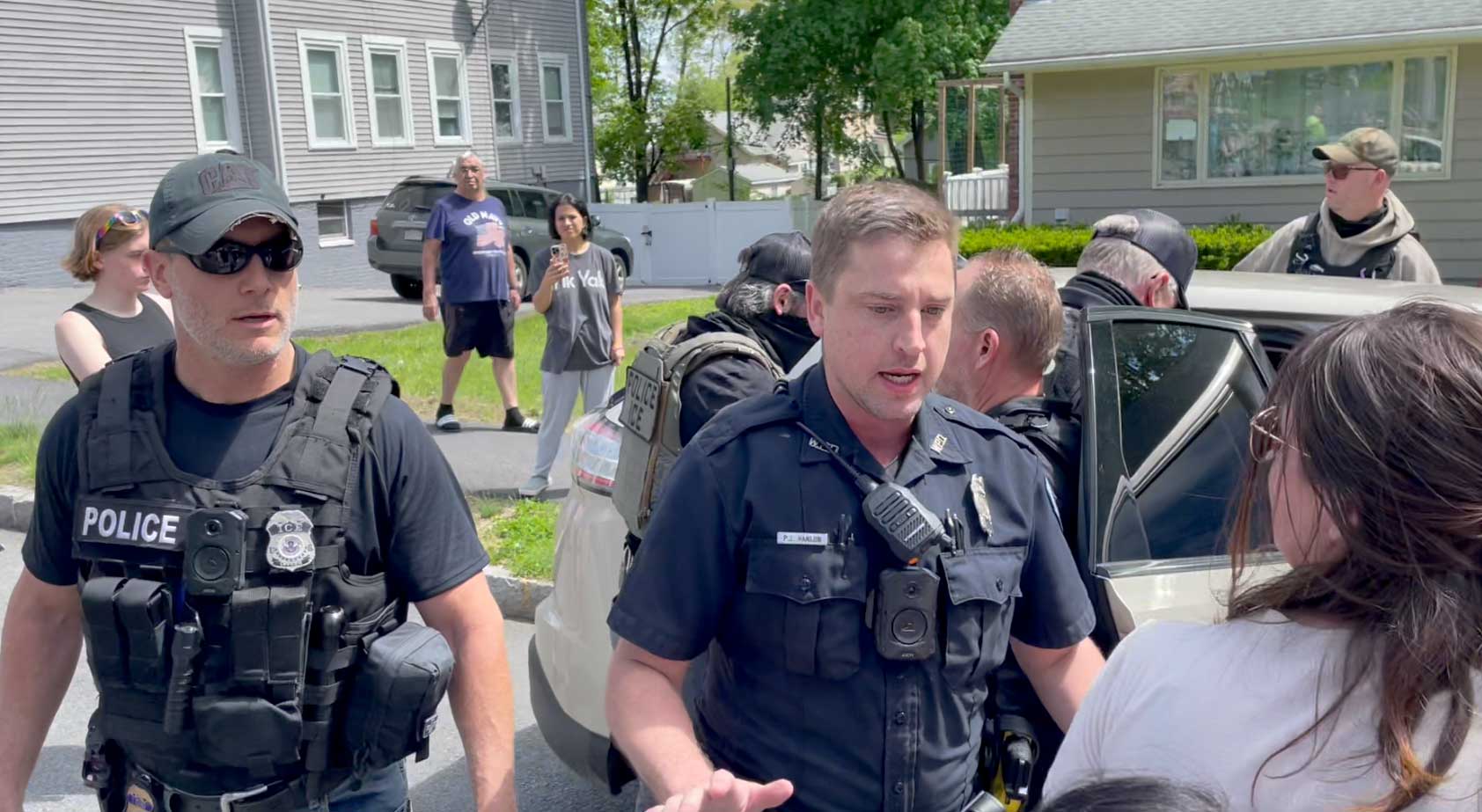 A Worcester police officer stands between the ICE agents and a crowd of community members.